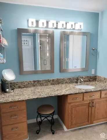 Dual framed vanity mirrors, natural stone-finish countertop, wood-finish cabinetry, and a single undermount sink
