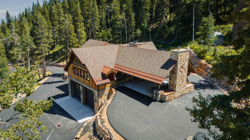 Stunning mountain residence featuring a steeply pitched composite shingle roof, stone chimney, and mixed wood and stone exterior cladding