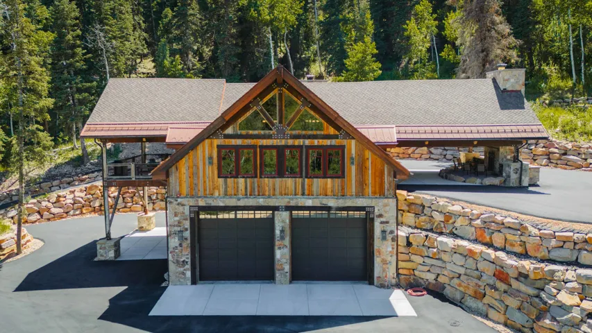 Rustic-modern exterior featuring stone and wood siding, a two-car garage, and a covered patio area with a stone fireplace