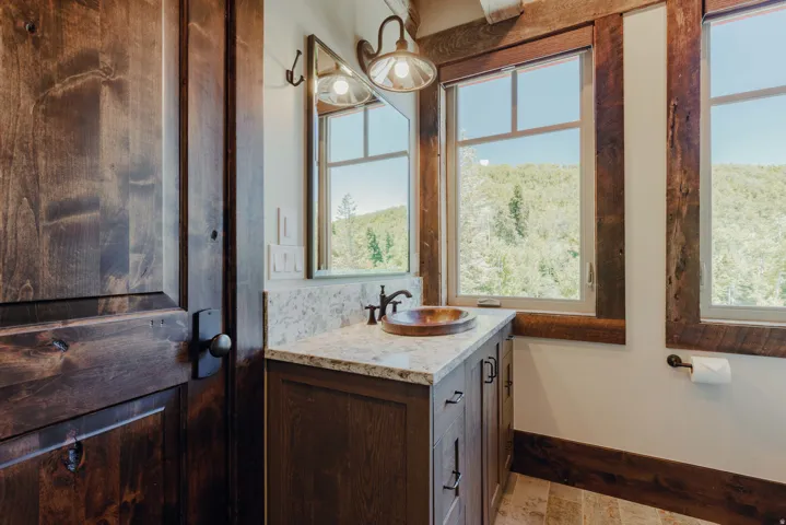 Bathroom vanity featuring a vessel sink, stone countertop, wood-finish cabinetry, and framed mirror