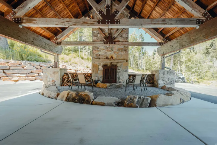 Covered outdoor living space featuring a stone fireplace, wood-beamed ceiling, and a concrete patio