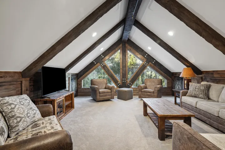Vaulted ceiling with exposed wood beams, expansive triangular windows, recessed lighting, wood-paneled walls, and carpeted flooring