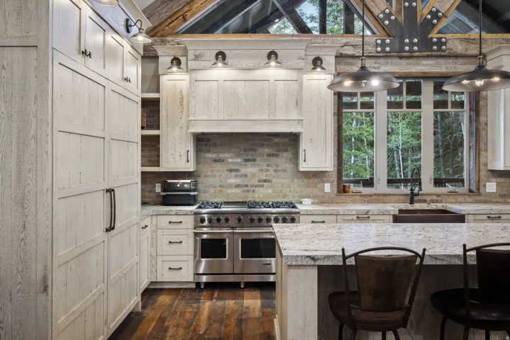 Gourmet kitchen featuring a professional-grade stainless steel range, light wood-finish cabinetry, stone countertops, a brick-patterned backsplash, and rich wood-finish flooring