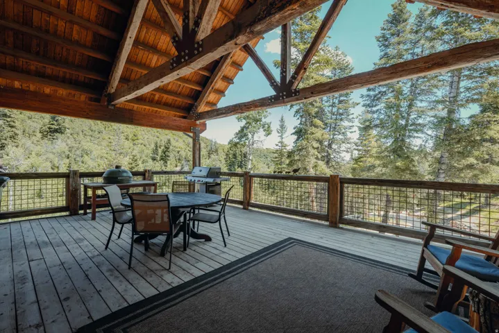 Expansive covered deck with exposed timber framing, wood plank flooring, and metal grid railings