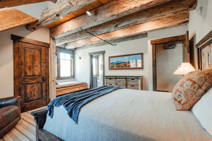 Exposed wood-beam ceiling with integrated lighting, rustic wood-paneled door, and a built-in window bench