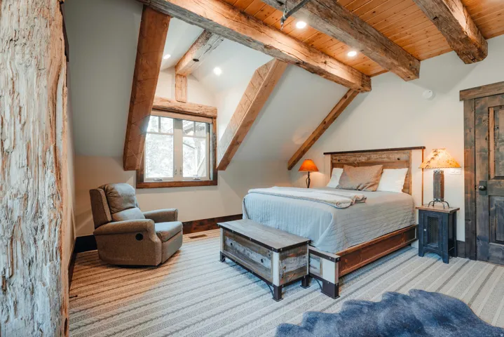 Charming attic bedroom showcasing exposed timber beam ceiling architecture, skylights providing natural illumination, and wood-finish flooring throughout