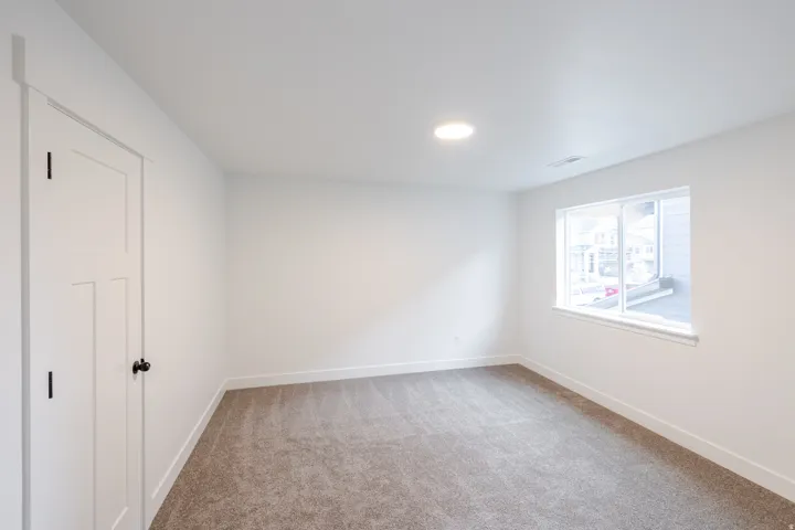 Neutral wall color, recessed ceiling light, white window trim, paneled interior door, and gray carpeting