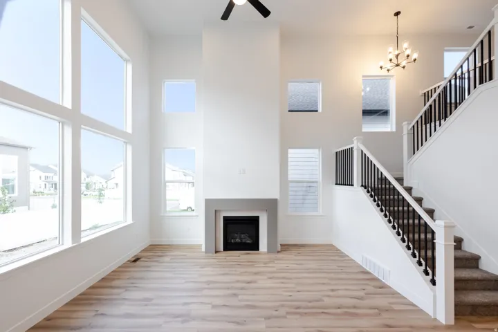Two-story living area featuring wood-finish flooring, a contemporary fireplace with a gray mantel, and a multi-level staircase with black metal balusters