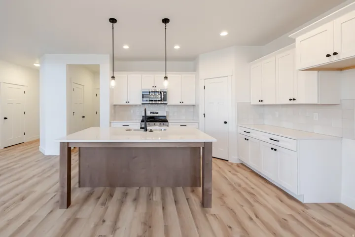 Bright kitchen featuring white shaker cabinetry, an island with integrated sink, stainless steel appliances, light-toned wood-finish flooring, and recessed ceiling lighting