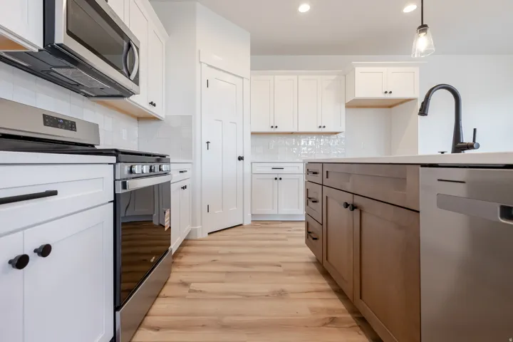 Kitchen featuring stainless steel appliances, white subway tile backsplash, light wood-finish flooring, and a two-tone cabinetry design