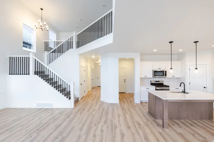Open-concept layout featuring wood-finish flooring, a kitchen island with stone countertop, and a double staircase with black railings