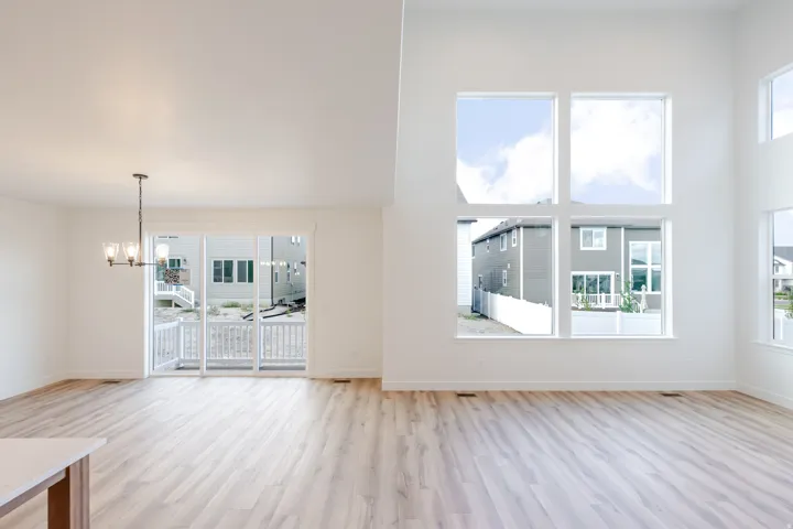 Expansive room featuring high ceilings, wood-finish flooring, a contemporary chandelier, multiple large windows, and a sliding glass door opening to an outdoor patio with a white railing