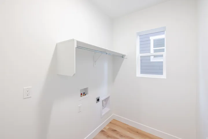 Laundry area with a built-in shelf and hanging rod, utility hookups, a white-framed window, and wood-finish flooring