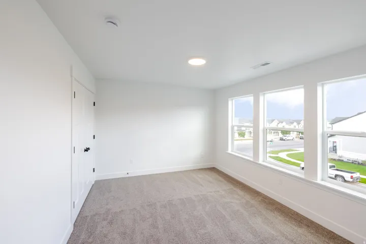 Bright interior space featuring three large windows, recessed ceiling lighting, textured carpeting, and a white paneled door with dark hardware