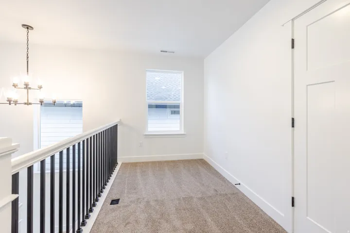 Carpeted landing featuring a contemporary chandelier, white walls, and a window providing natural light