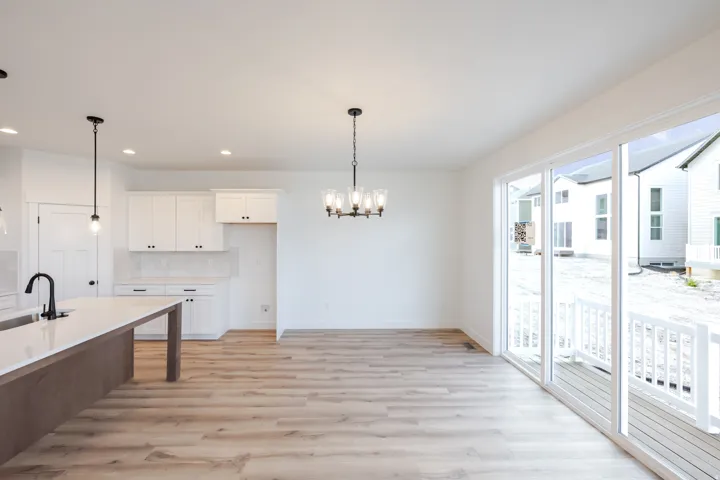 Open-concept living area featuring wood-finish flooring, white cabinetry, a kitchen island with an integrated sink, a contemporary chandelier, and a sliding glass door to an outdoor deck