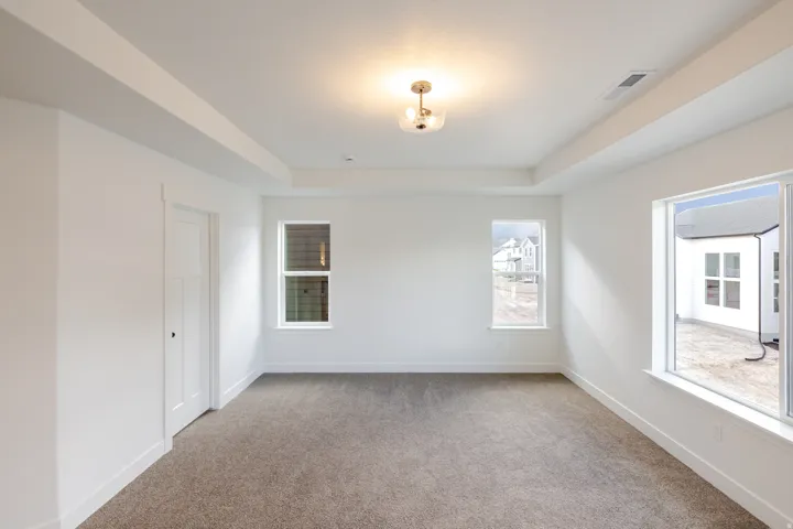 Tray ceiling with recessed lighting, integrated ceiling light fixture, white interior door with dark hardware, gray carpeting, and multiple windows