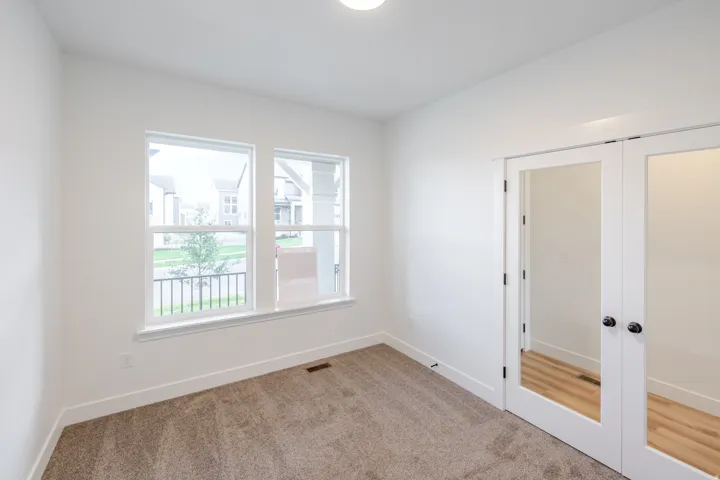 White walls, carpet flooring, two large windows, white trim, and French doors with glass panels