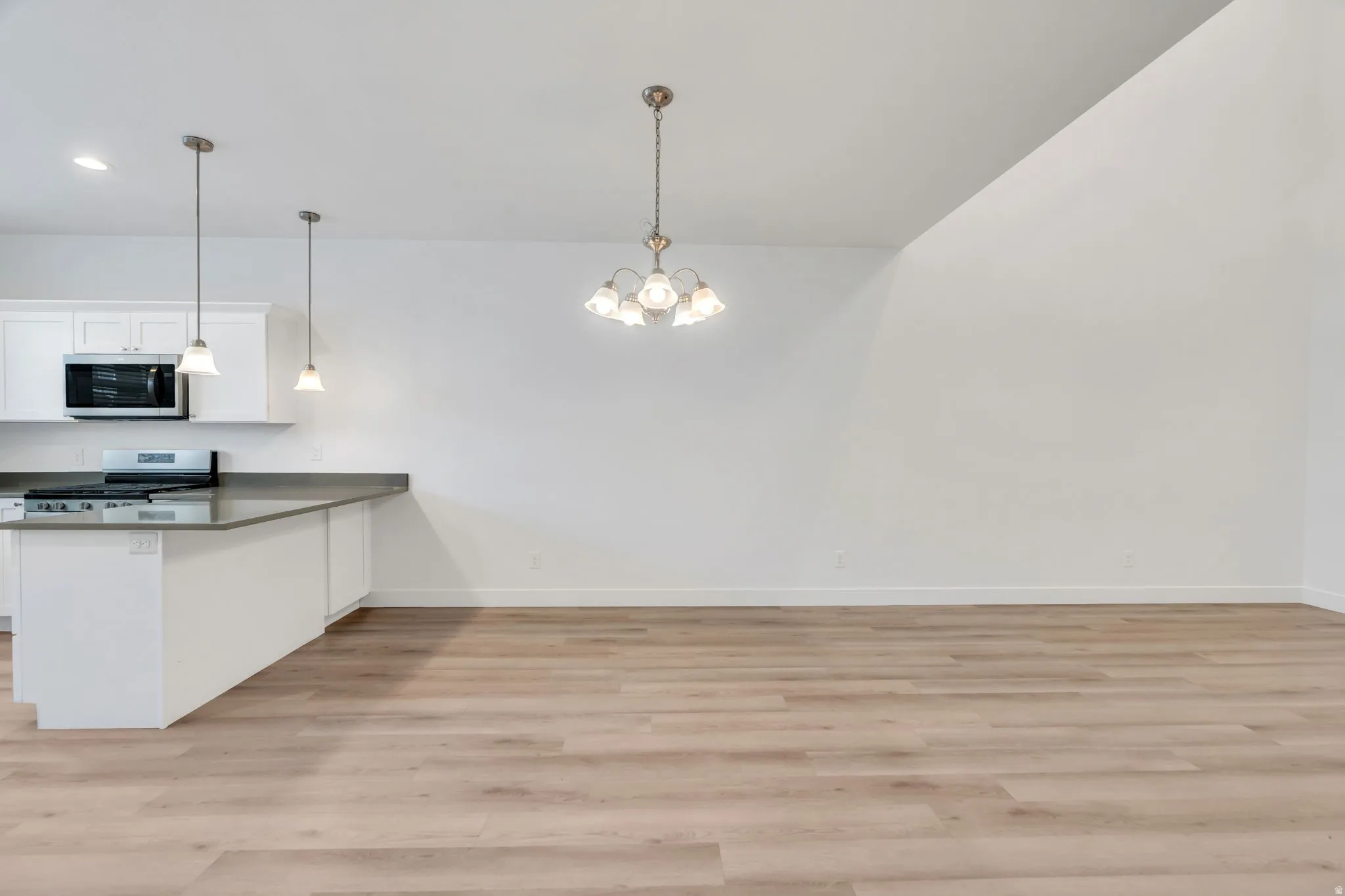 Open-concept living space with vaulted ceilings, wood-finish flooring, a kitchen island with stone countertops, white shaker cabinetry, and stainless steel appliances