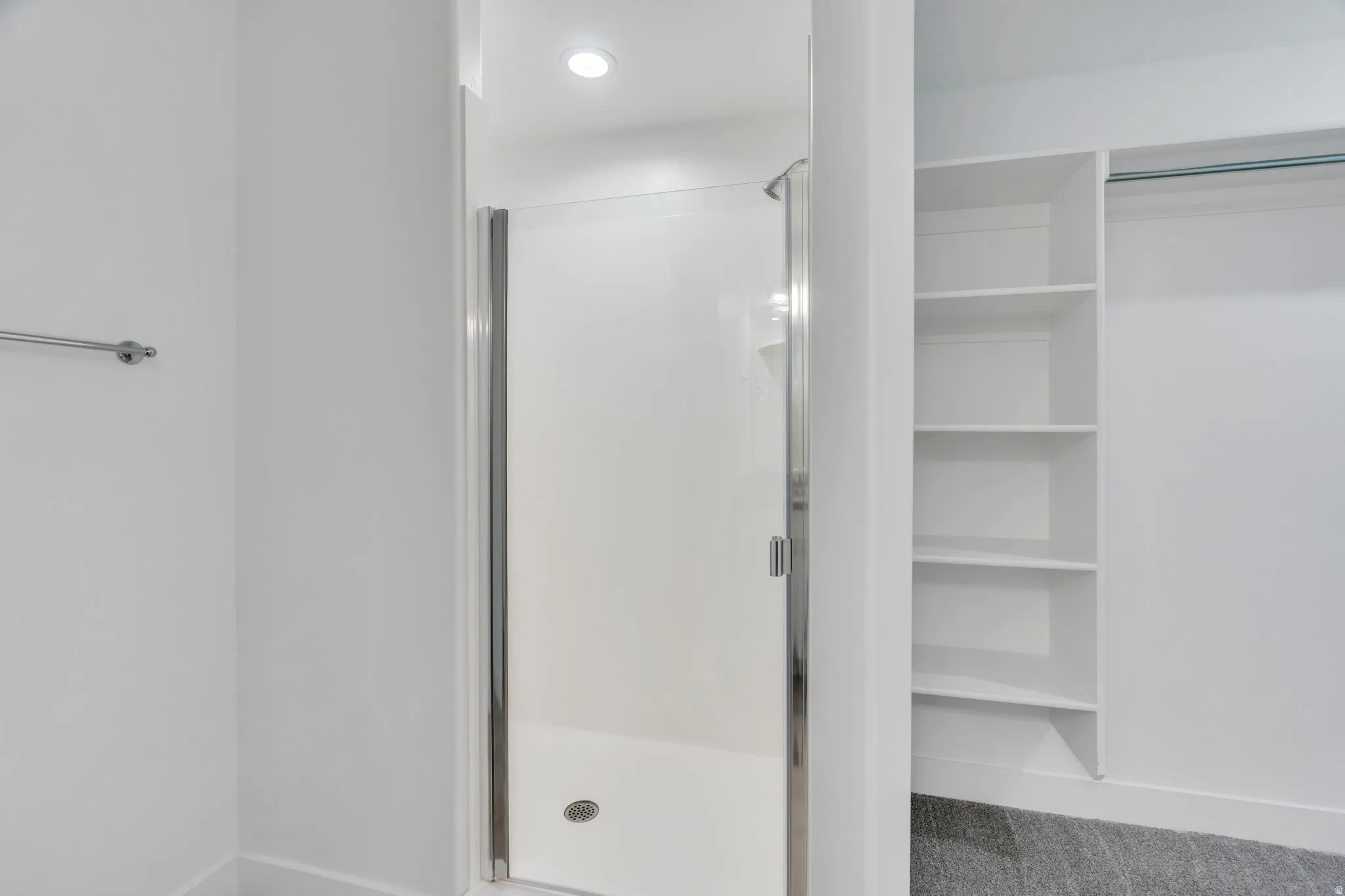 Walk-in shower with a chrome-framed glass door, recessed lighting, and a built-in shelving unit