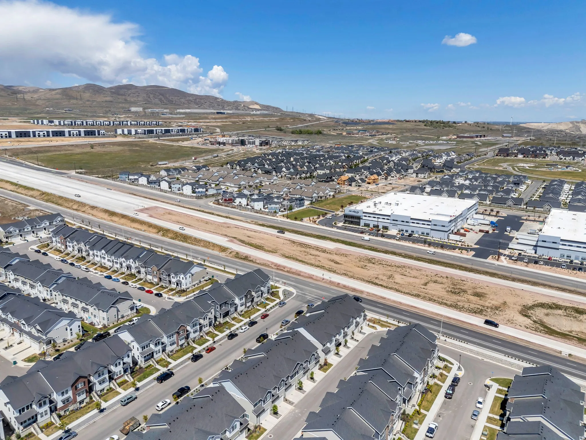 Expansive aerial showcasing a developing residential area with rows of multi-story townhomes, adjacent to a major roadway
