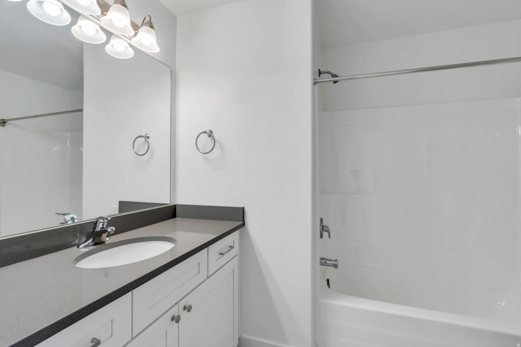 Bathroom featuring a spacious vanity with an undermount sink, a large mirror, white cabinetry, a dark countertop, and a shower-tub combination