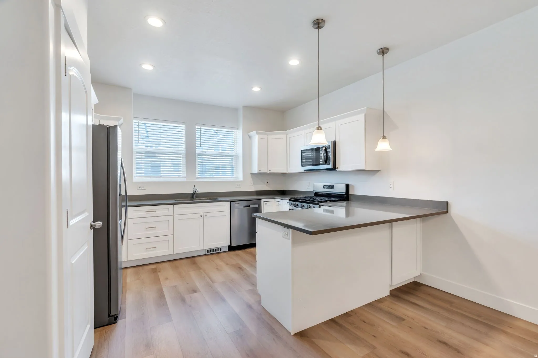 Kitchen featuring white shaker cabinetry, stainless steel appliances, wood-finish flooring, recessed lighting, and pendant lighting