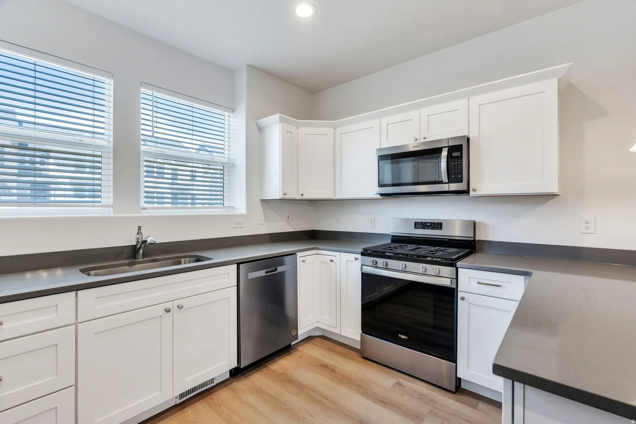 Kitchen featuring white cabinetry, grey countertops, stainless steel appliances, and wood-finish flooring