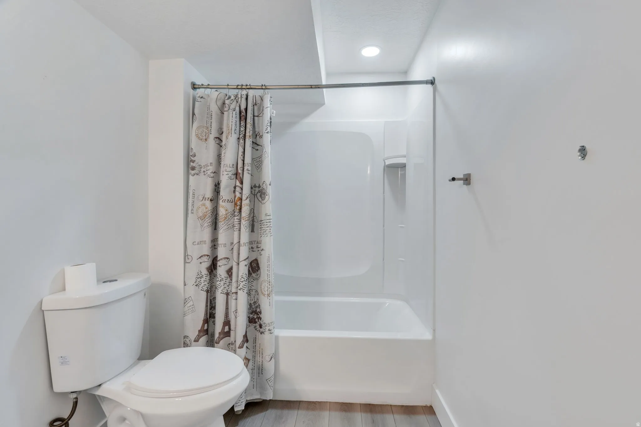 Bathroom featuring a white toilet, integrated shower and bathtub unit, wall-mounted towel bar, and recessed lighting
