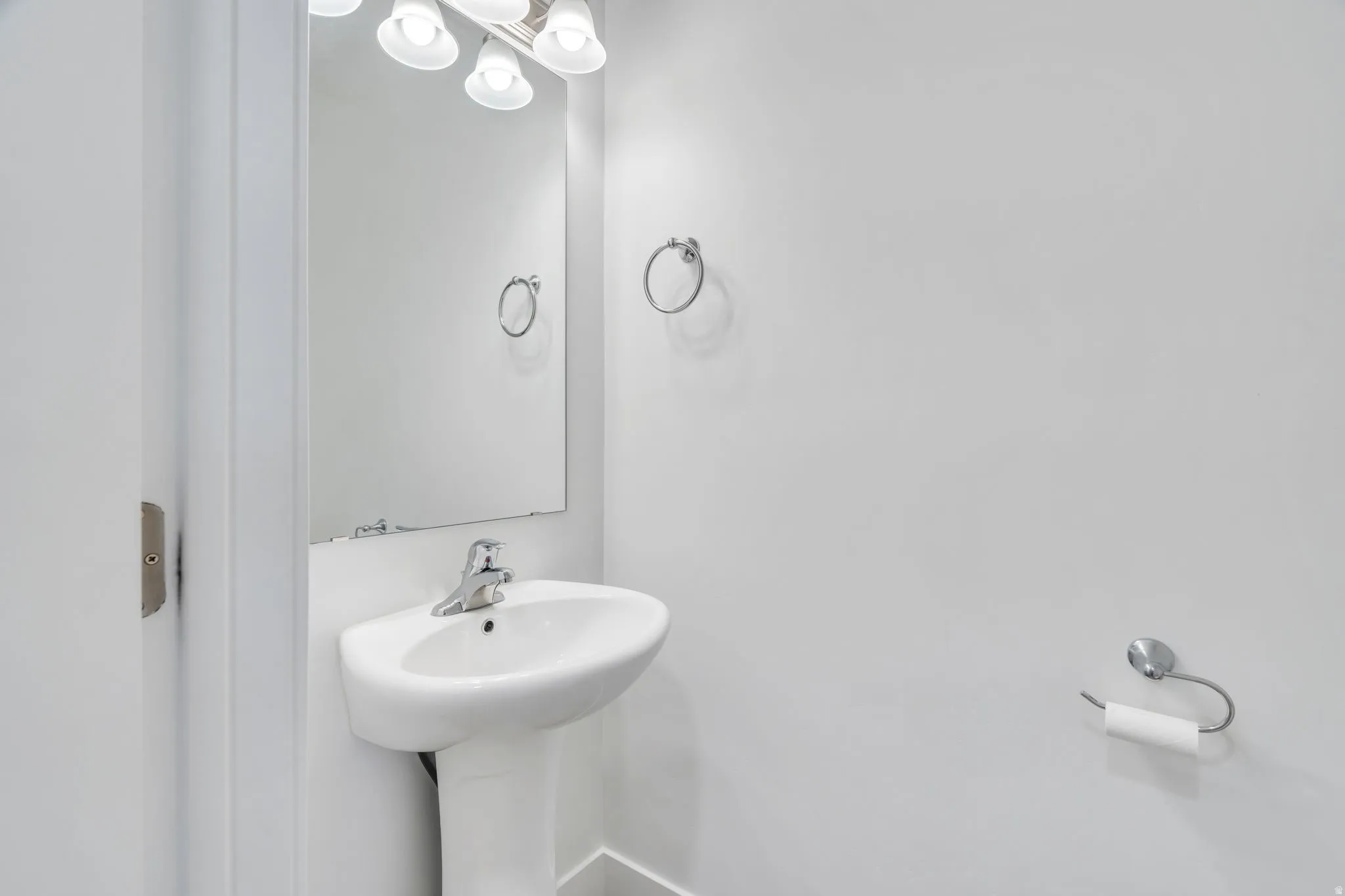 Pedestal sink with chrome faucet, wall-mounted mirror, and vanity lighting