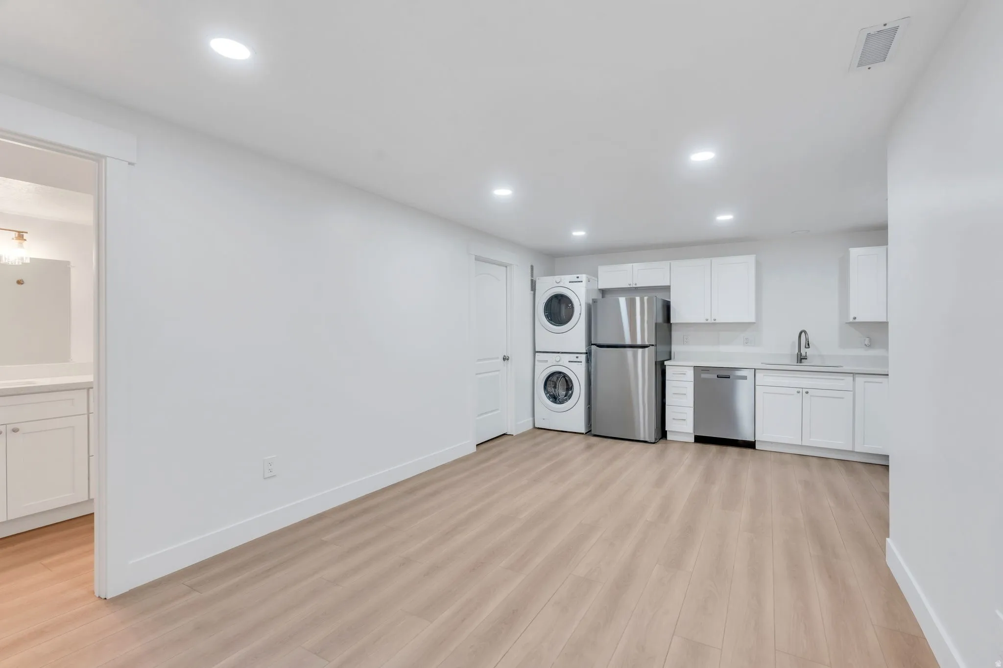 Open-concept living space featuring wood-finish flooring, recessed lighting, and a full kitchen with white cabinetry, stainless steel appliances, and a stacked washer and dryer
