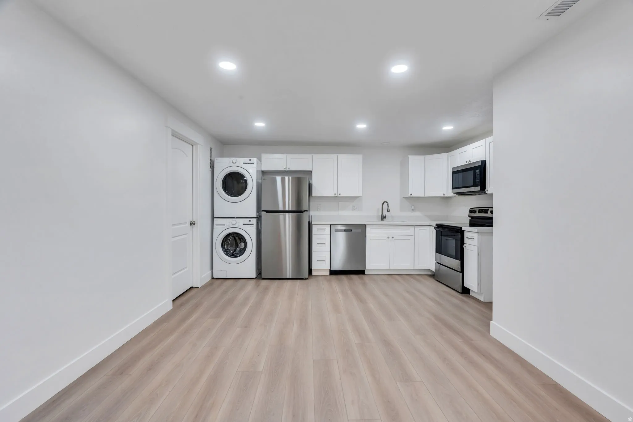 Open-concept kitchen area featuring light wood-finish flooring, white cabinetry, and stainless steel appliances