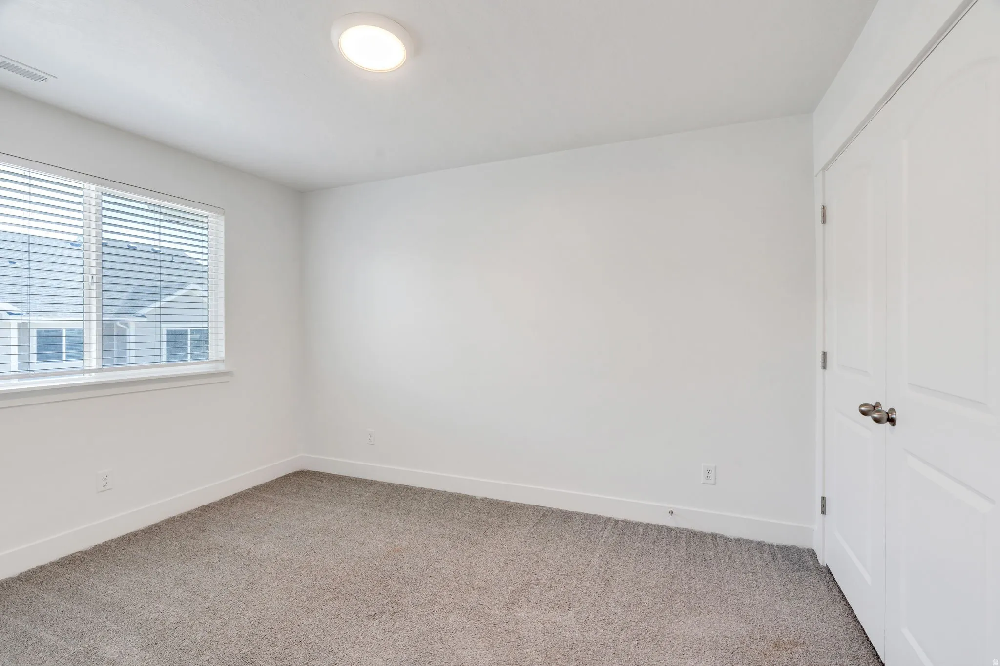 Carpeted room featuring a double-pane window with blinds, white walls, and a ceiling-mounted light fixture
