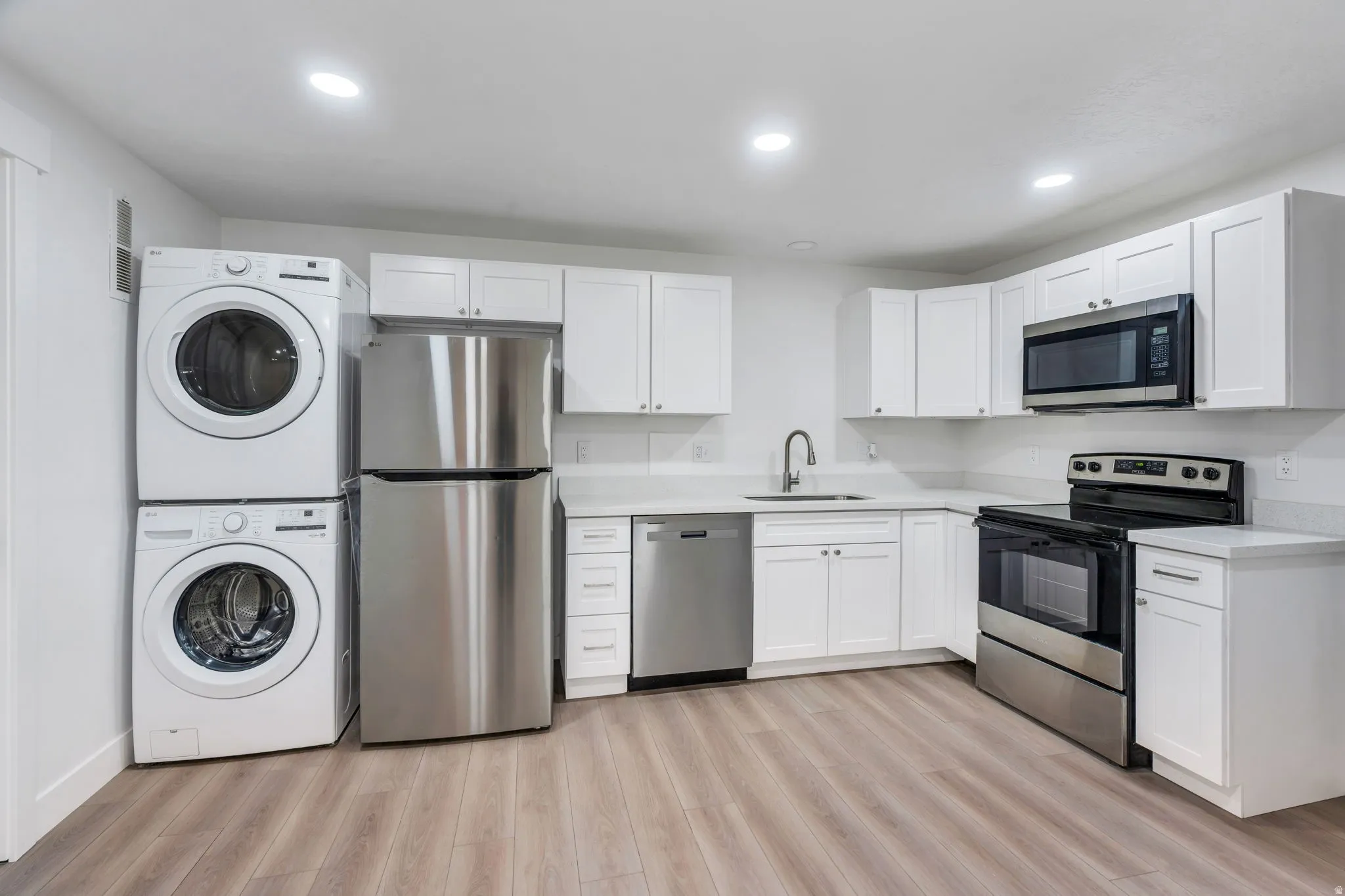 Modern kitchen space featuring white cabinetry, light-toned countertops, and wood-finish flooring