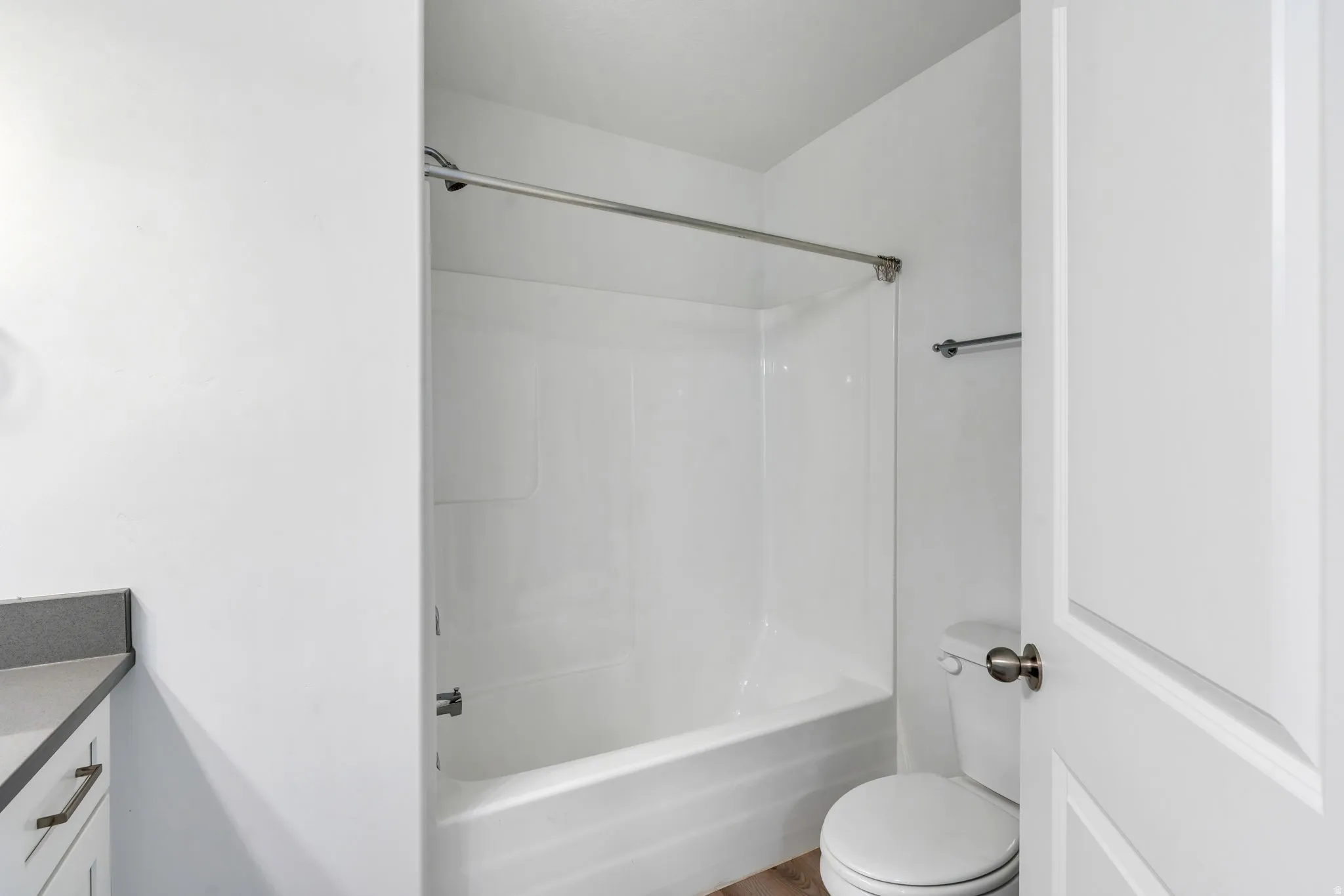 Bathroom featuring a white bathtub/shower combination with a chrome shower rod, a white toilet, and a vanity with a dark countertop and white cabinetry