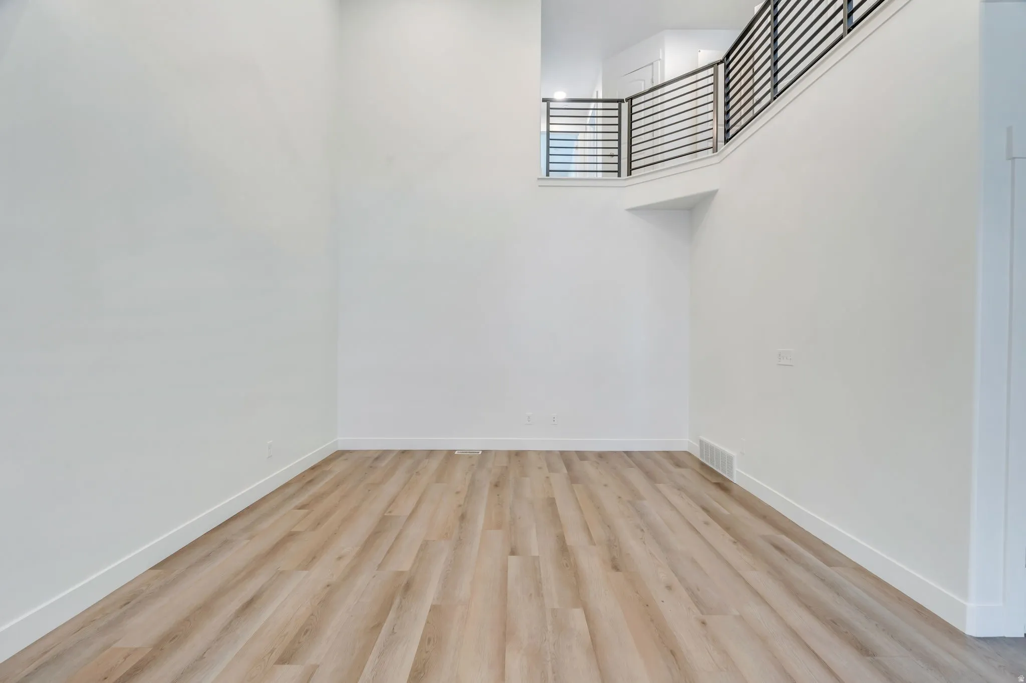 Spacious living area featuring light wood-finish flooring and crisp white walls