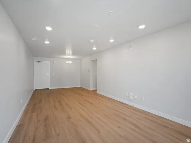 Spacious room featuring wood-finish flooring, recessed lighting, a chandelier, and a white entrance door