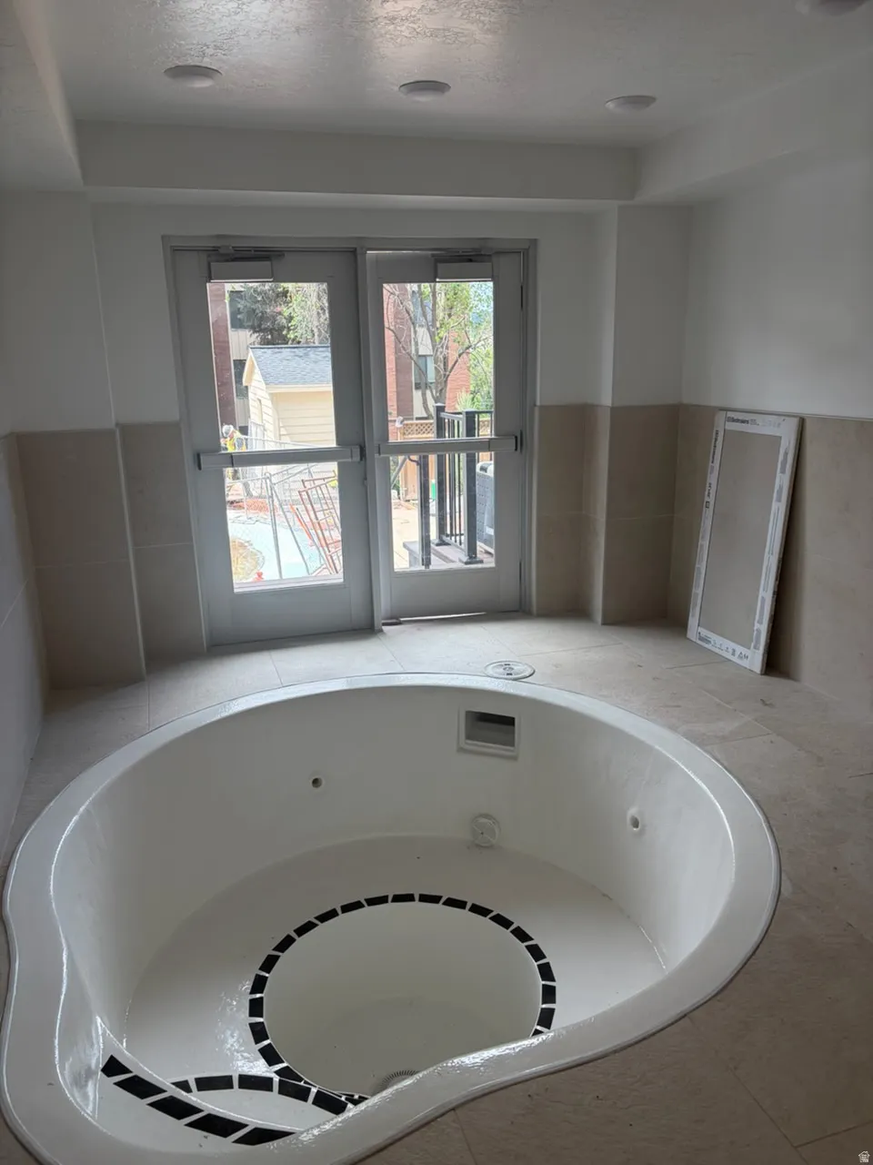 Built-in soaking tub with black accent tile, surrounded by neutral-toned floor tile and wainscoting