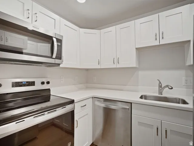 Contemporary kitchen featuring white shaker cabinetry, stainless steel appliances, a stainless steel sink, and light-toned countertops