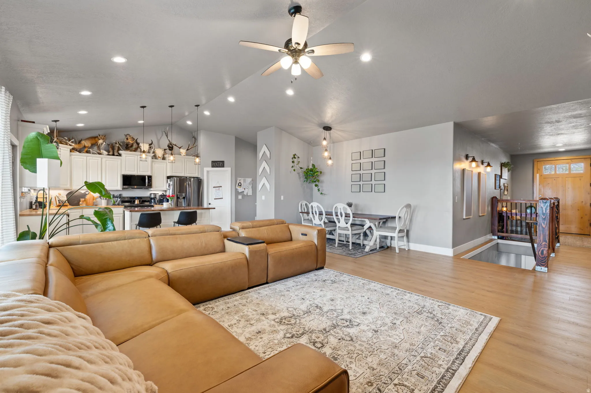 Expansive open-concept living area featuring light wood-finish flooring, a contemporary ceiling fan with integrated lighting, recessed lighting, and a defined dining space
