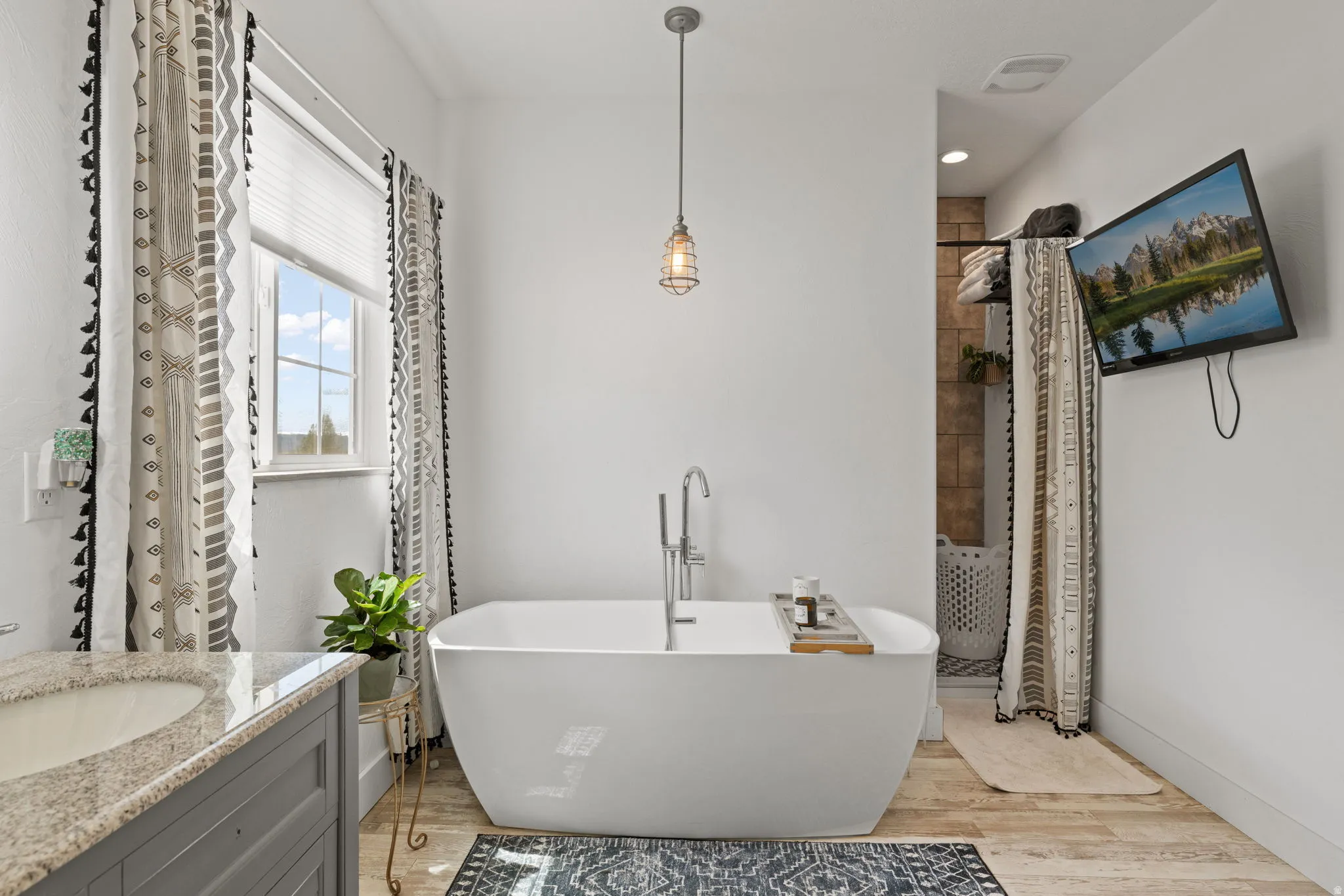 Primary Bedroom with en-suite, spacious bath featuring a freestanding soaking tub with floor-mounted faucet, wood-finish flooring, an inset window, and a built-in vanity with a light-toned countertop and undermount sink