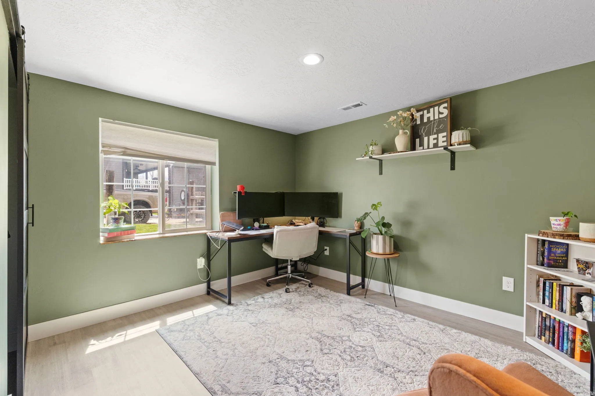 Spacious basement bedroom featuring light wood-finish flooring, a contemporary ceiling light fixture, and a window with natural light