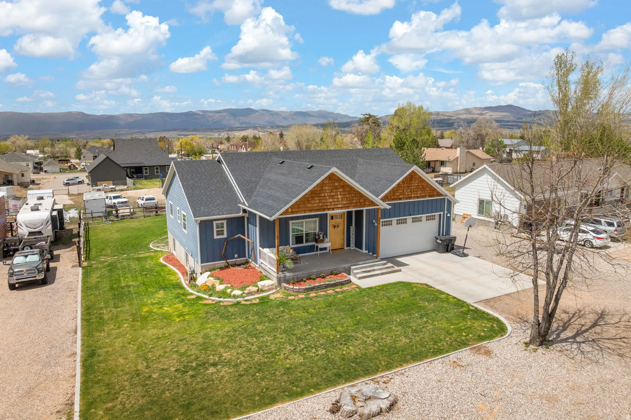 Blue siding exterior featuring a covered porch, an attached two-car garage, a concrete driveway, a manicured lawn, and natural landscaping with red mulch accents