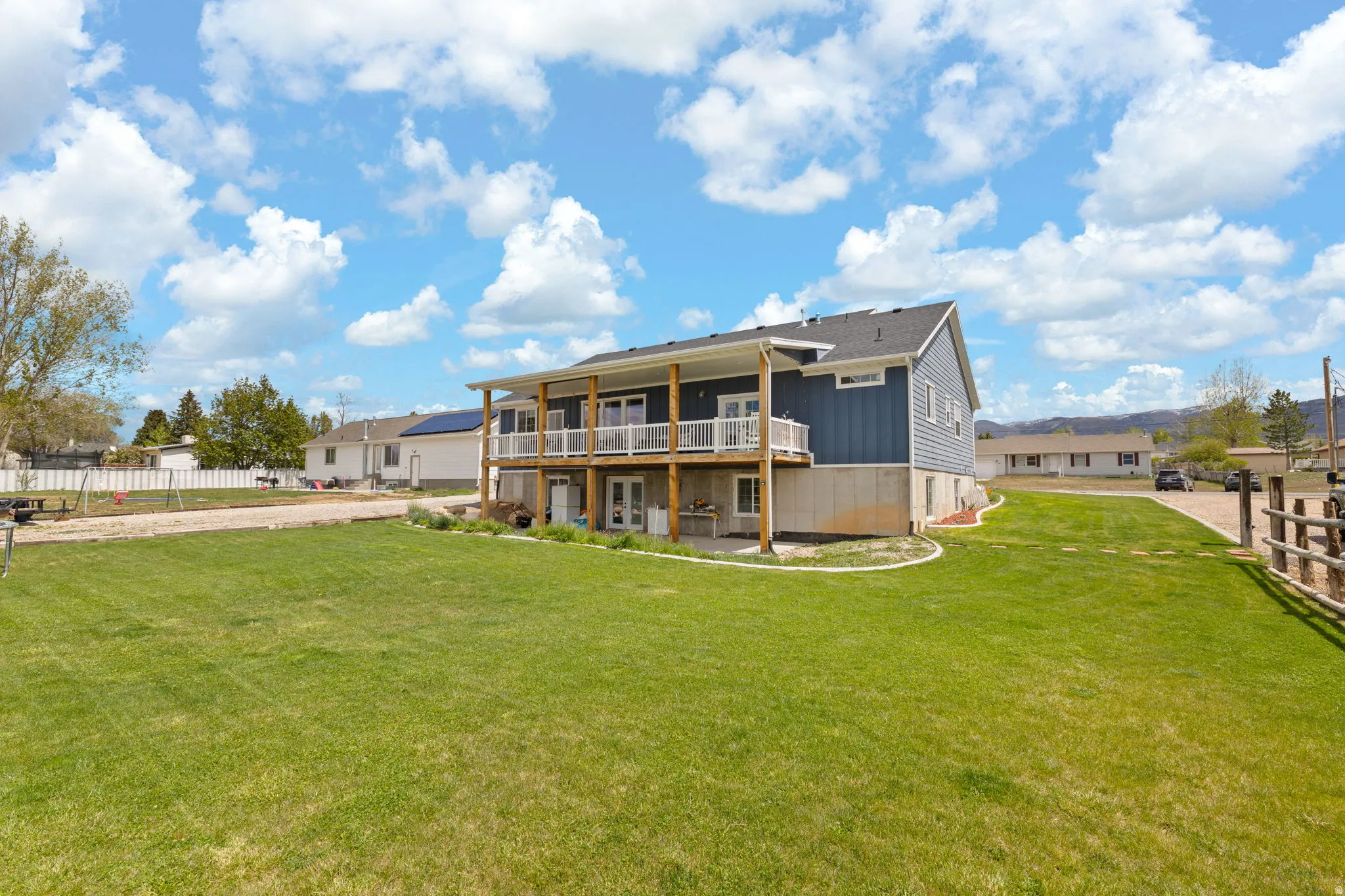 Expansive green lawn bordering a two-story residence with a full-width upper-level deck, lower-level patio access, and blue horizontal siding