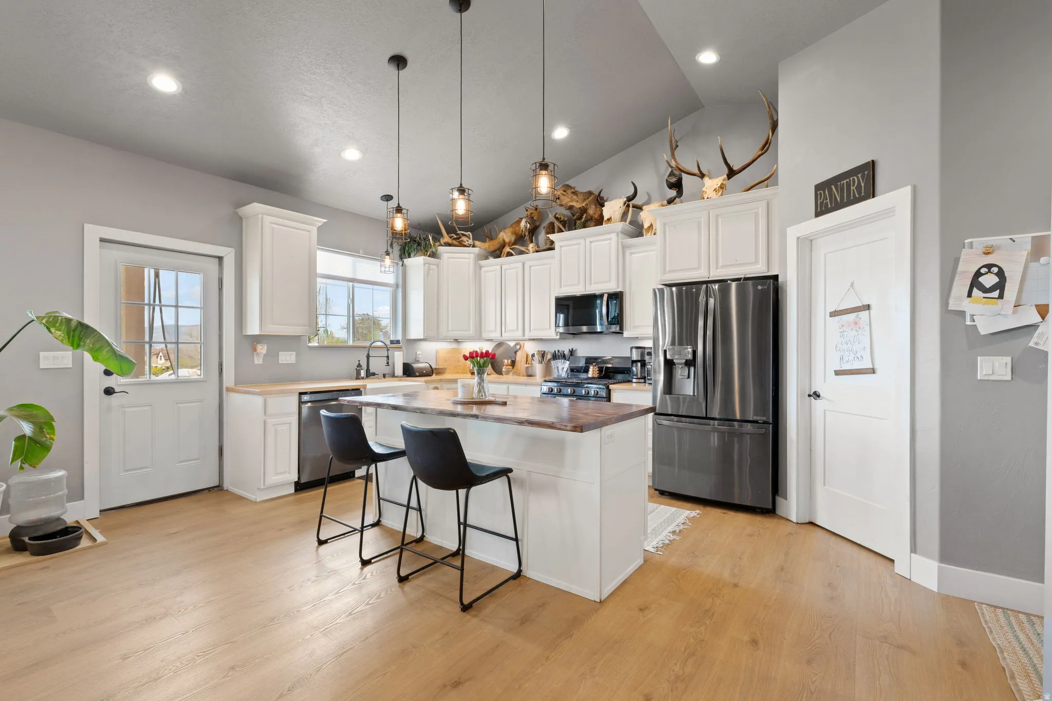 Bright kitchen featuring wood-finish flooring, white cabinetry, stainless steel appliances, and a central island with bar seating
