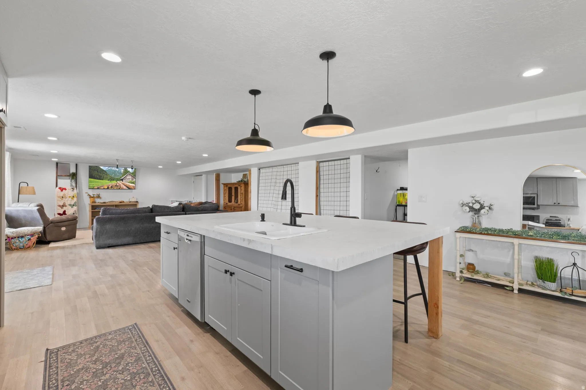 Basement ADU, open-concept lower level featuring a central island with a dual-basin sink and matte black faucet, light wood-finish flooring, recessed lighting, and stylish pendant fixtures