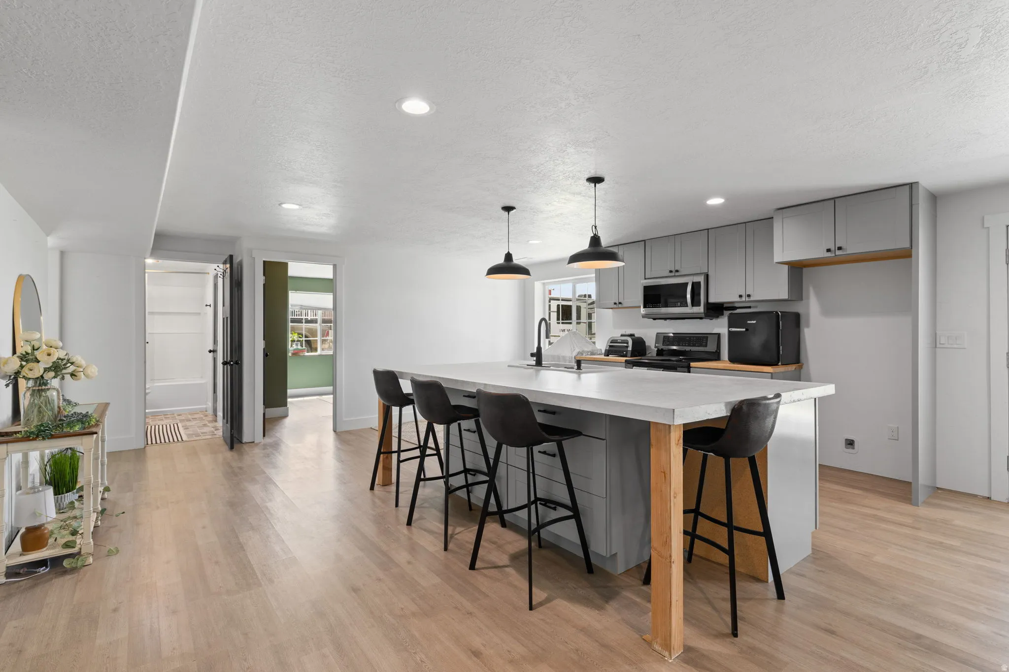 Spacious 2nd kitchen featuring an expansive center island with seating, pendant lighting, light gray cabinetry, built-in microwave, and wood-finish flooring