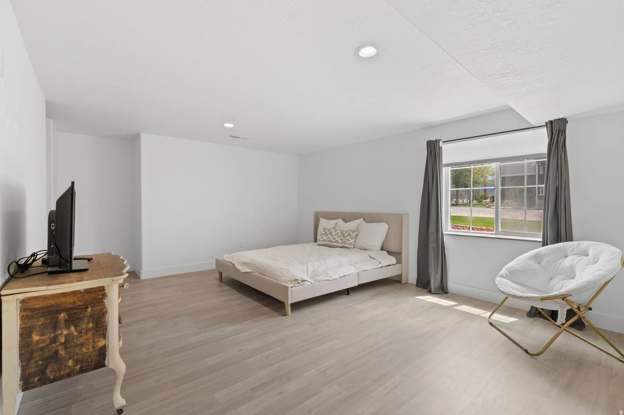 Spacious basement bedroom featuring wood-finish flooring, recessed lighting, and a large window providing ample natural light