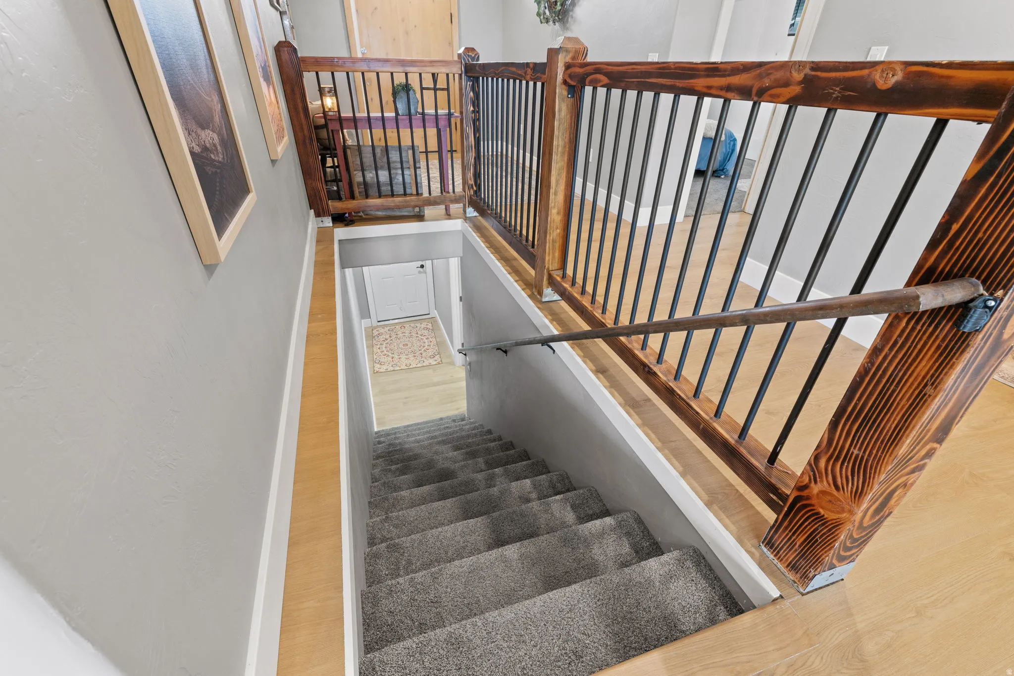 Stairwell featuring a dark wood-finish railing with black metal balusters, carpeted steps, and wood-finish flooring