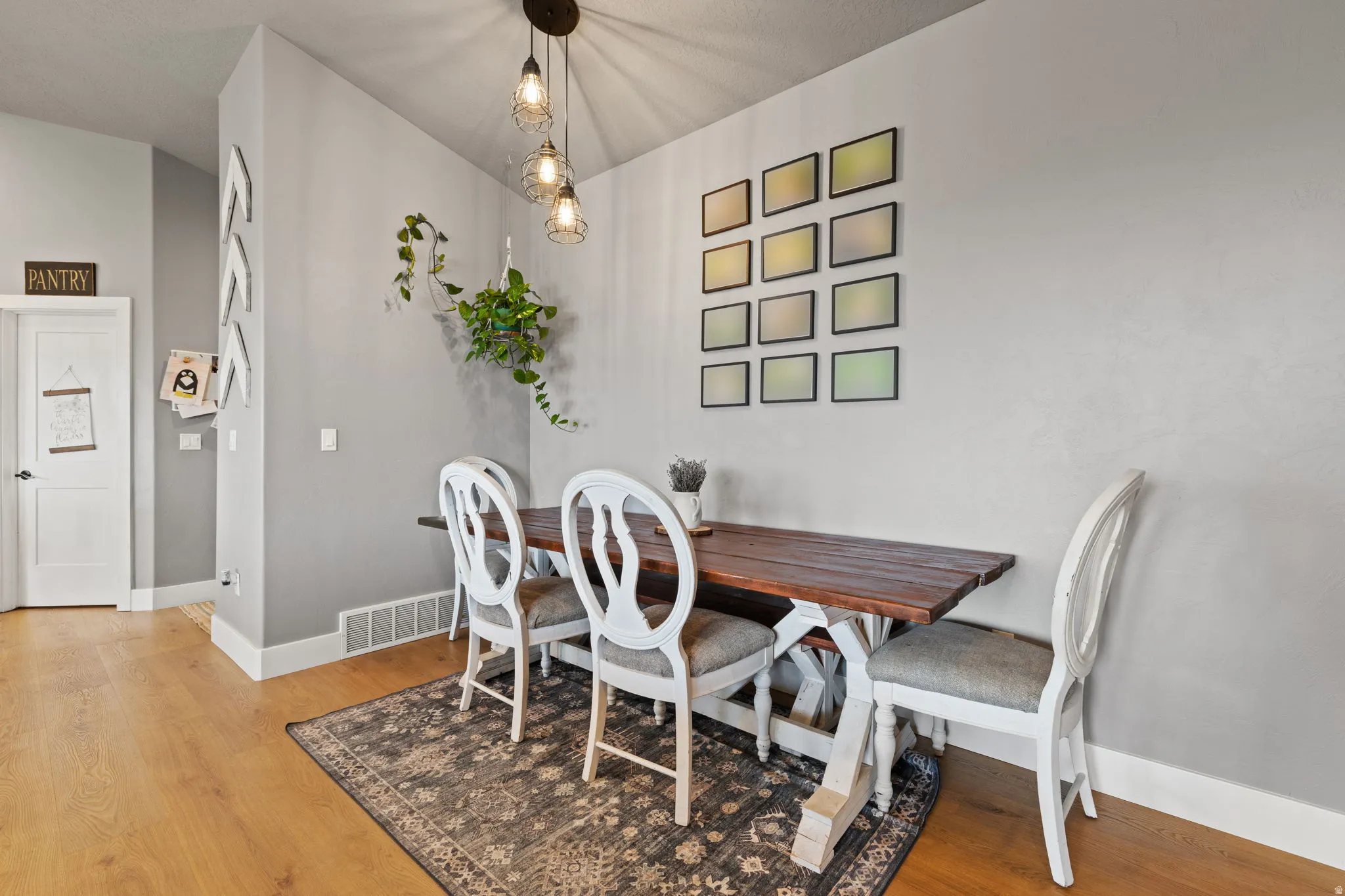 Dining area featuring wood-finish flooring, a contemporary chandelier with three pendant lights, and light gray wall paint